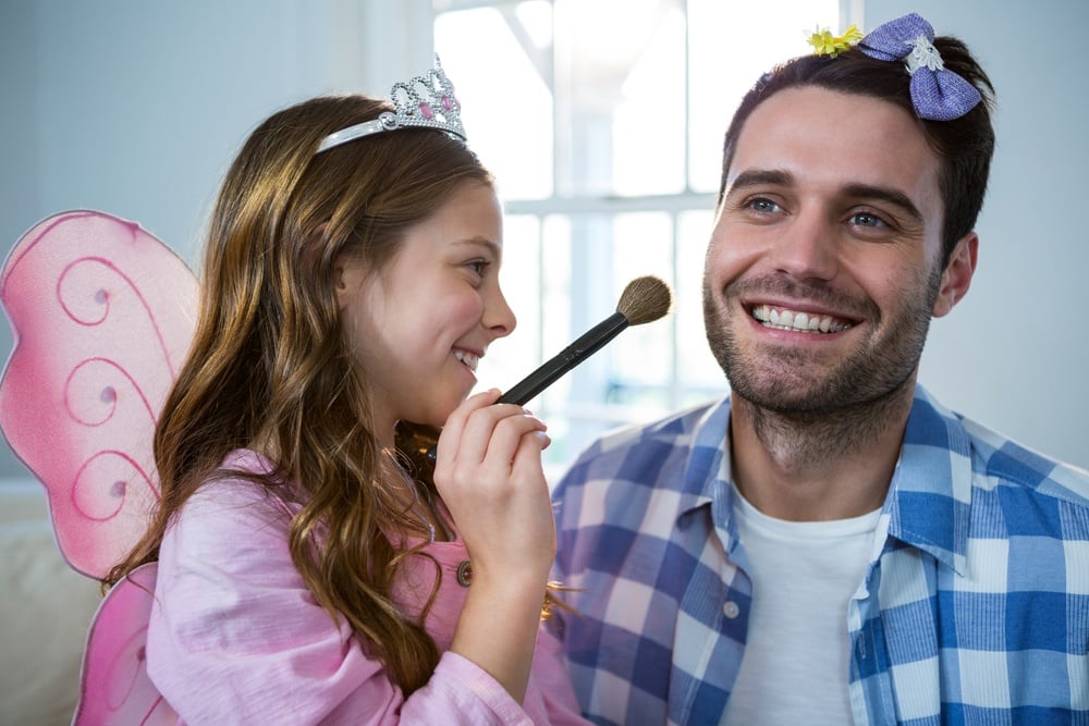 Girl dressed up in a fairy costume applying make-up on fathers face at home